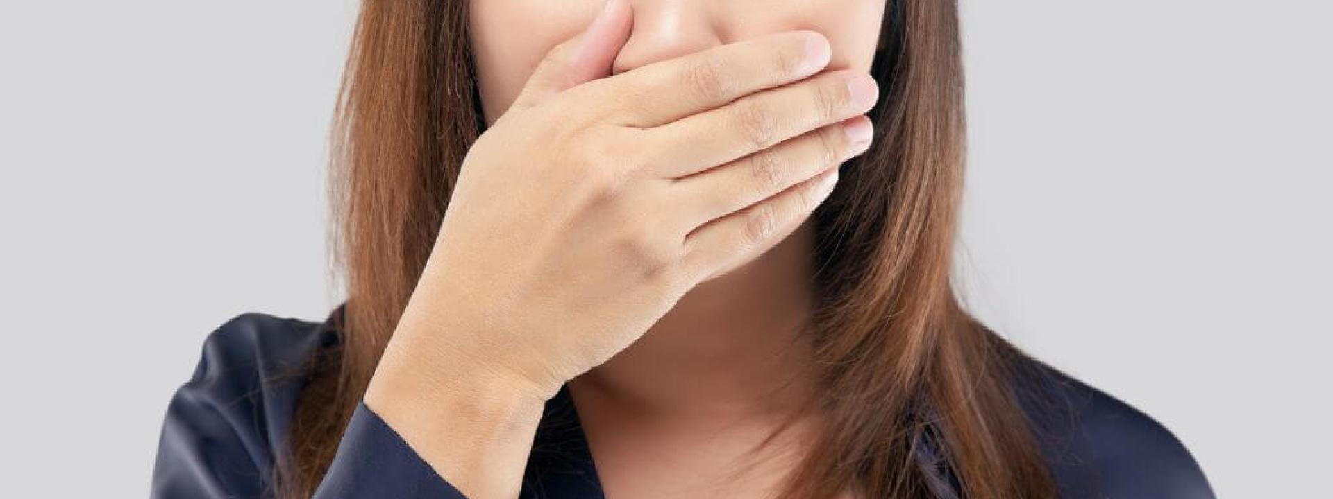 Woman covering her mouth due to bad breath, halitosis